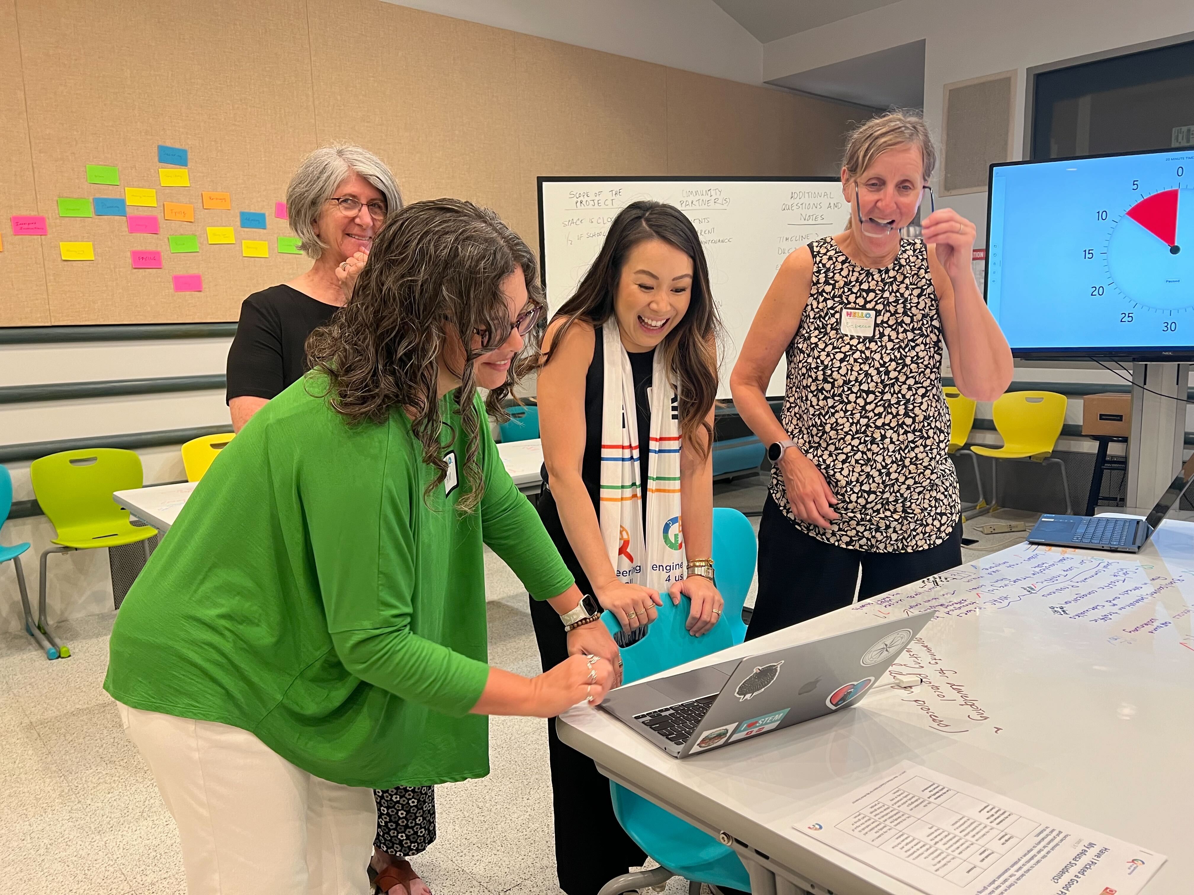 PL director in an in-person PD with three e4usa teachers around a table looking at a laptop