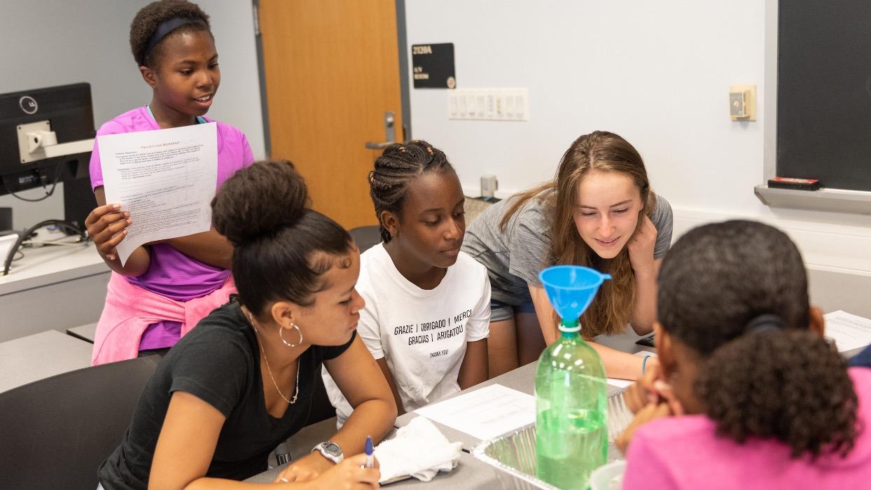 Students and a teacher gathering around a table in class