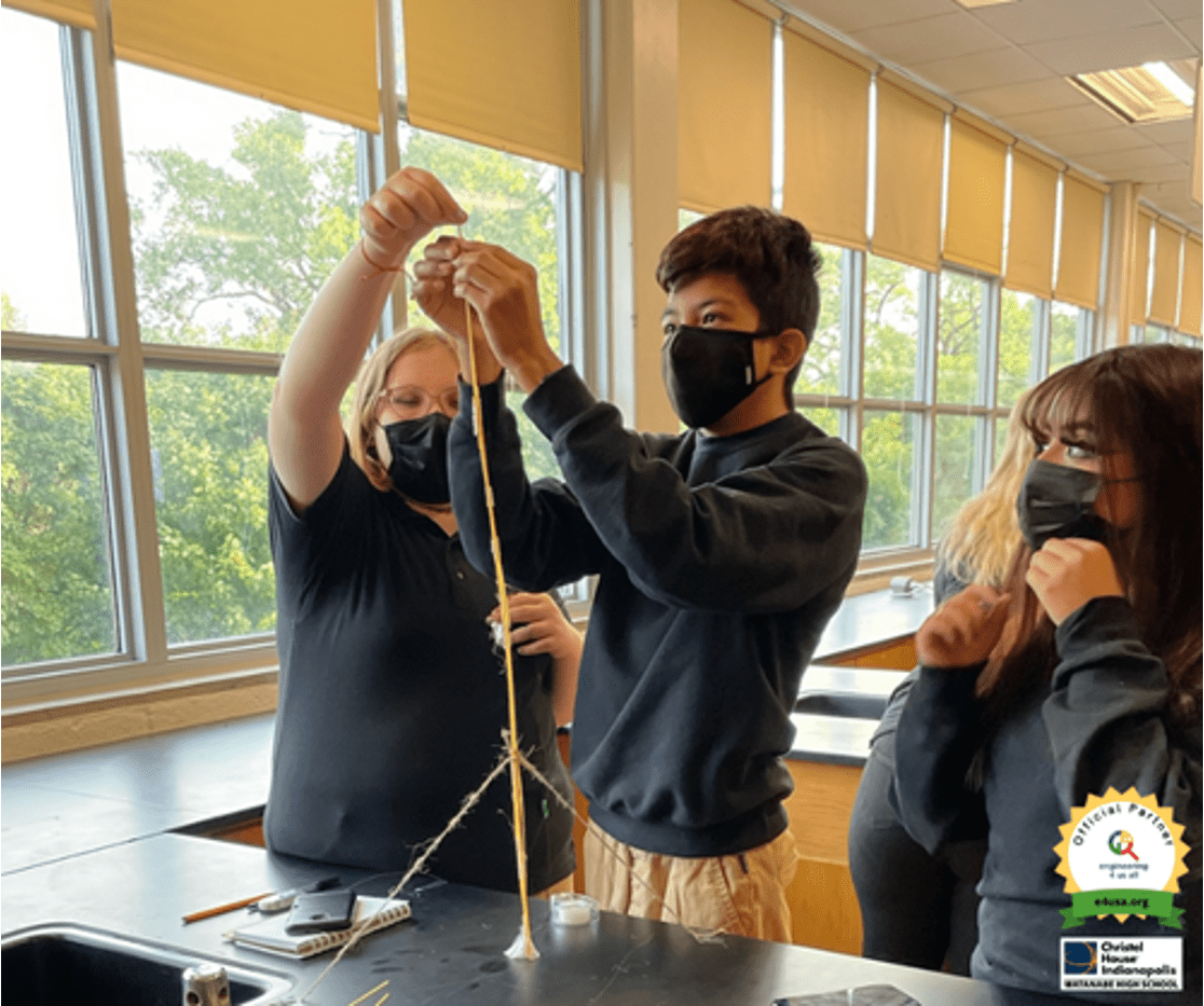 A teacher and 2 students building a tower structure in class.