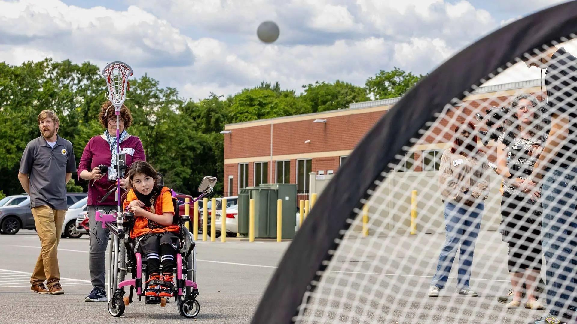 Stella Stakolosa scores with an adaptive lacrosse stick engineered by College Park Academy students under the guidance of teacher Brendan McCarthy (left), as part of the Engineering for Us All program.  Photo by John T. Consoli