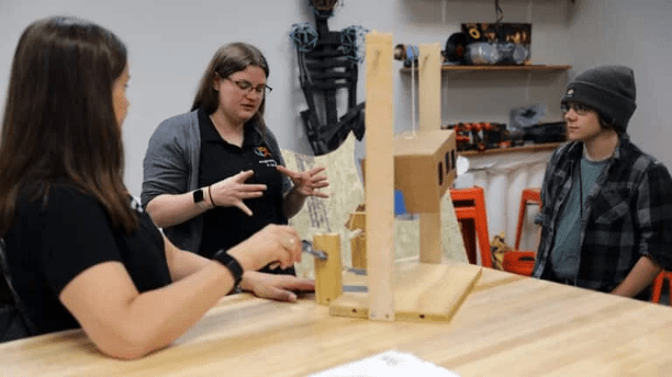 three people around table with wooden model.