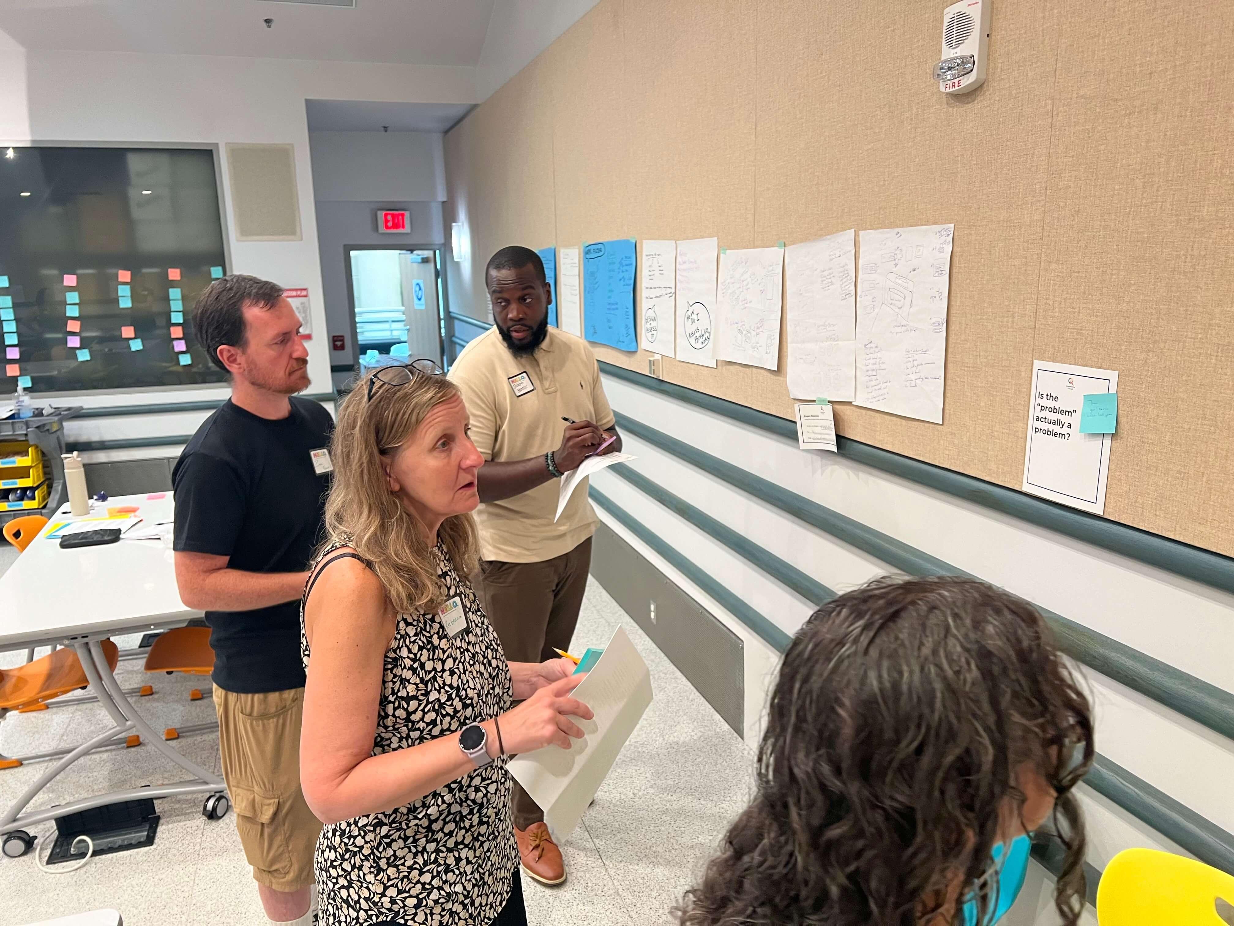Educators review sketches and notes displayed on a classroom wall.