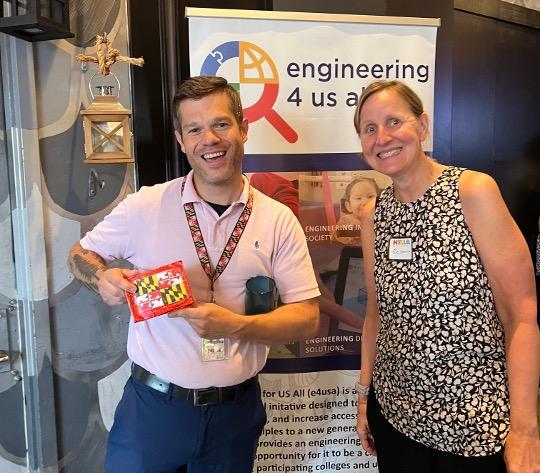 Two educators smile in front of an Engineering for US All banner.