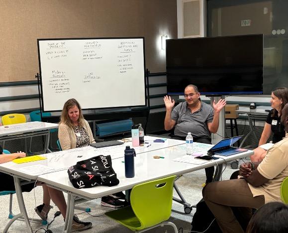 Educators participate in a group discussion around a classroom table.