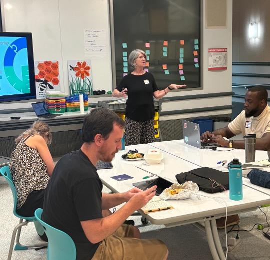 A facilitator speaks while educators work at tables during a workshop.